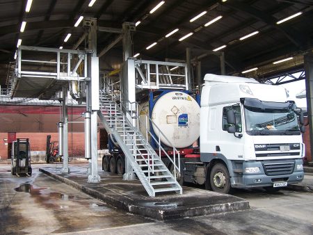 Two Carbis elevated truck platforms are separated by a ladder in a picture of a tanker bay. A tank truck is parked underneath one of them.