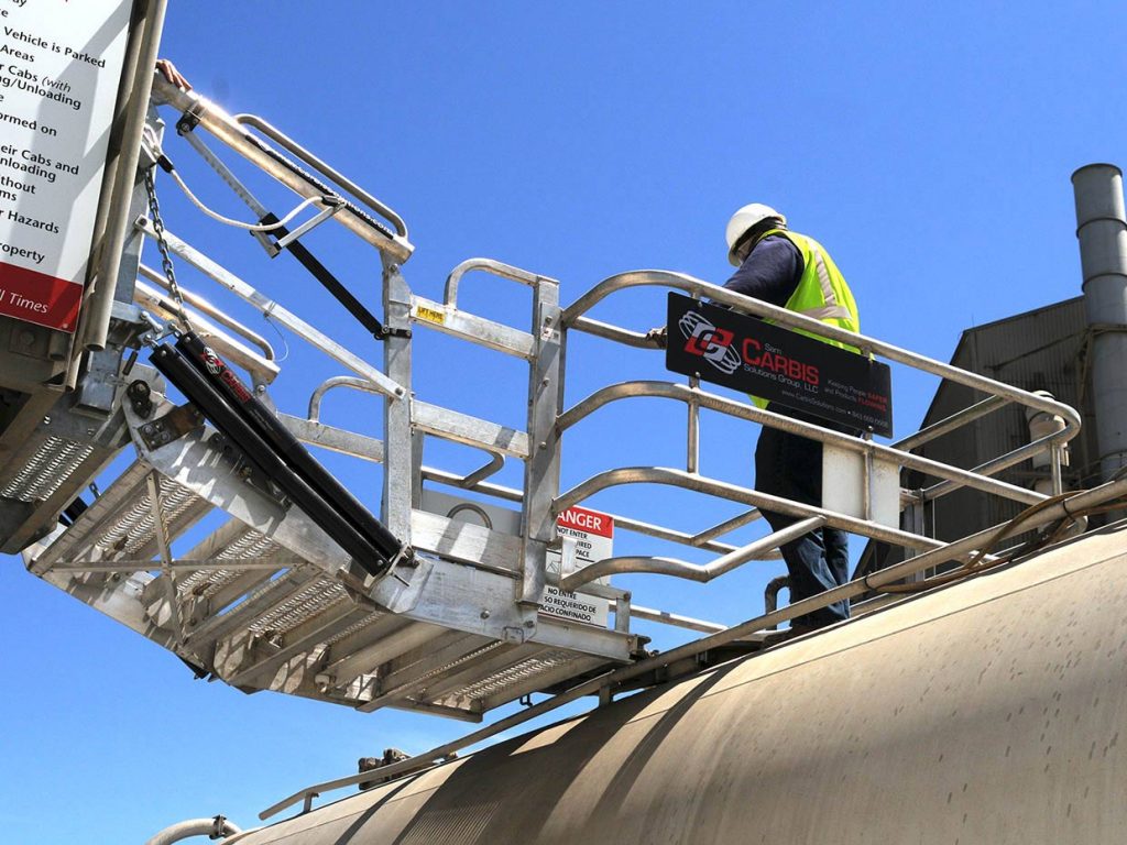 A man stands in a folding stairs gangway on top of a tanker car.