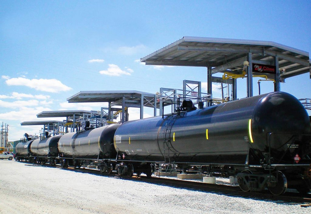 Multi-hatch loading bays tower over tanker railcars on a track.