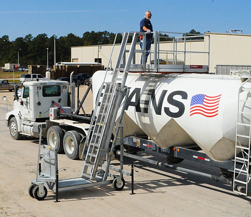 A Carbis portable tanker truck access system is pulled up onto a tank car with a man on the unit.