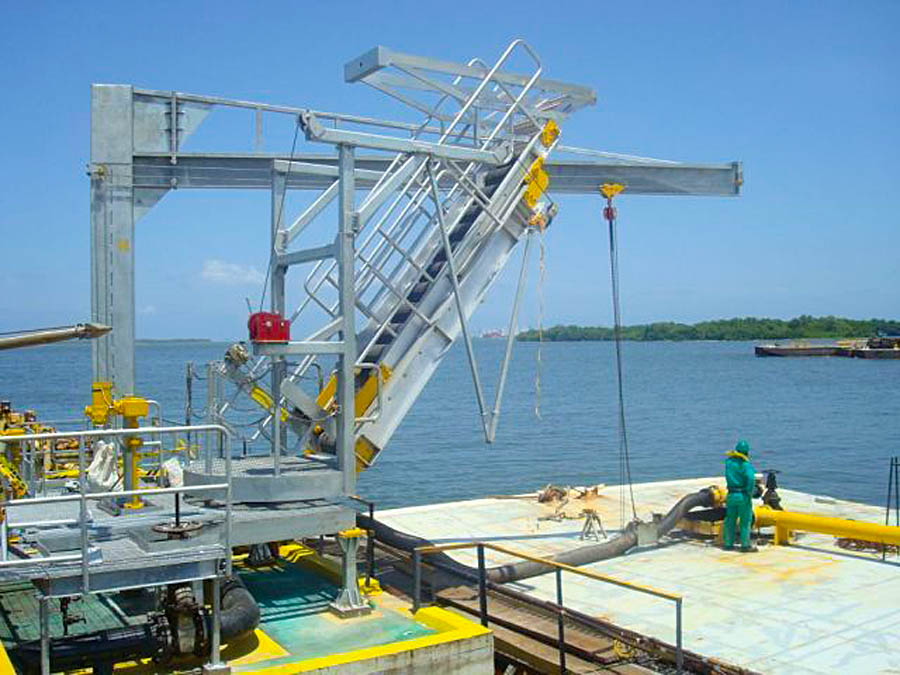 A hoist marine gangway extends over a barge.