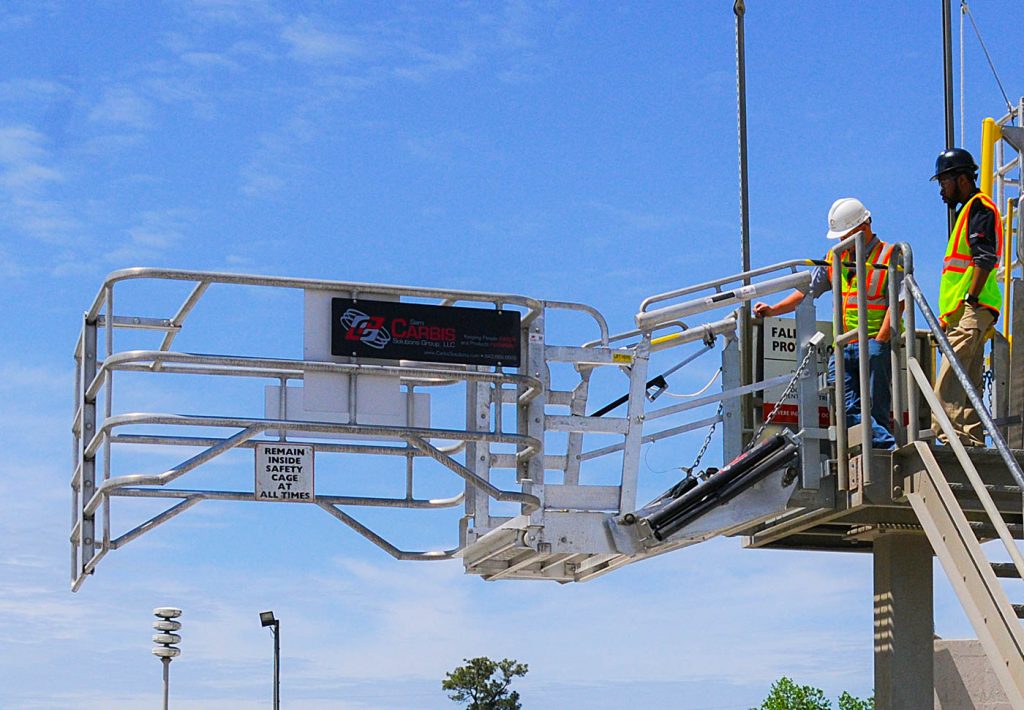 A worker stands on a Carbis Solutions folding stairs gangway enclosure above a tanker car.