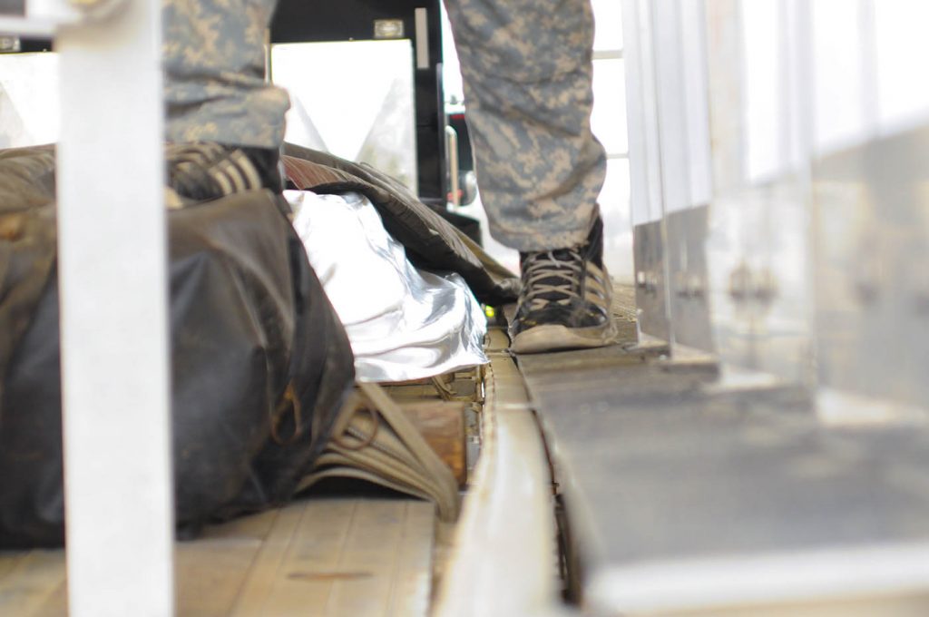 A man's feet are seen by the tarping. He's standing on the edge of the tarping platform and the flatbed itself.