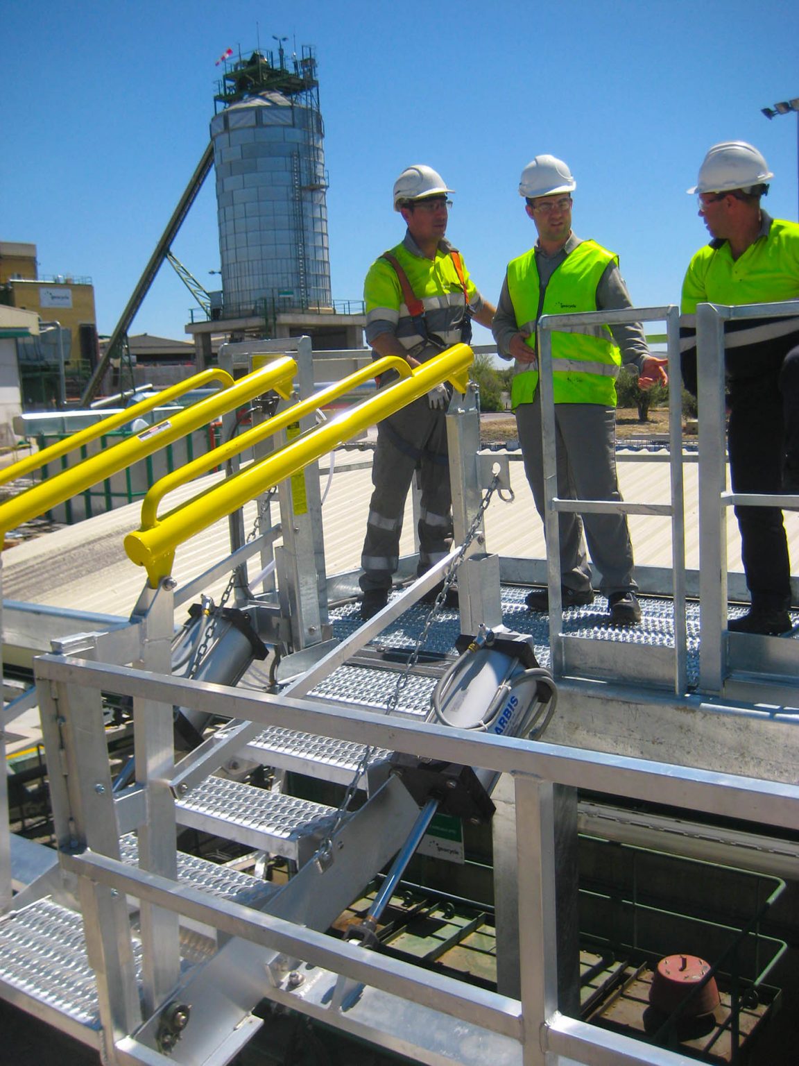 Workers stand on a Carbis Solutions folding stairs gangway enclosure above a tanker car.