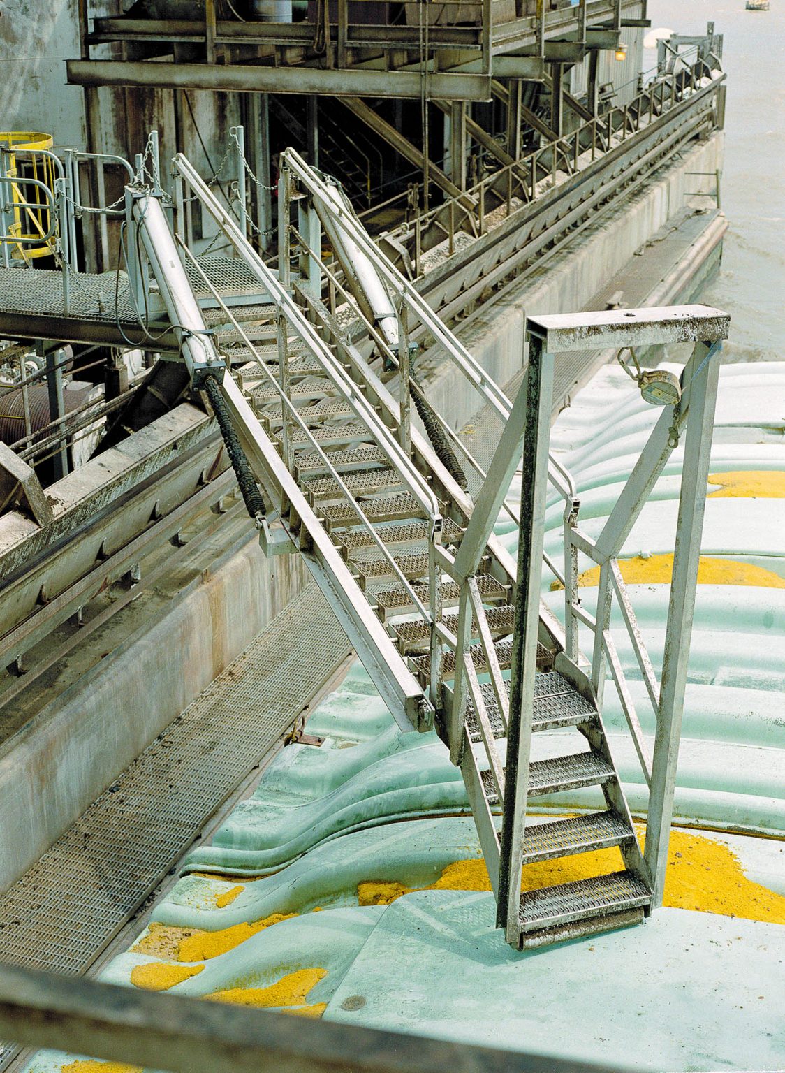 A telescoping marine gangway extends from a ship to a barge.